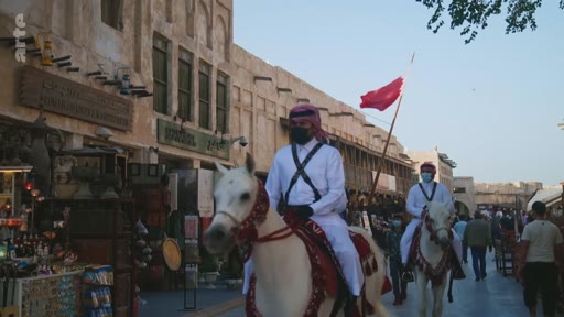 Des membres de la police montée qatarienne, vêtus de tenues traditionnelles, patrouillent à cheval dans les allées du souk Waqif à Doha, au Qatar. Cette scène illustre la présence des forces de l'ordre dans ce lieu touristique emblématique de la capitale qatarienne.