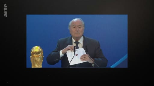 Sepp Blatter, alors président de la FIFA, dévoile le nom du Qatar comme pays hôte de la Coupe du monde de football 2022 lors d'une conférence de presse officielle. Le trophée de la Coupe du monde est visible à ses côtés.