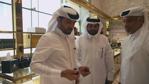 Trois hommes portant la thobe et le ghutra visitent une boutique de luxe au Qatar, examinant des produits de parfumerie ou de cosmétique. La scène illustre le commerce de détail haut de gamme dans la région du Golfe.