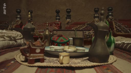 Un plateau traditionnel arabe disposé sur un tapis, comprenant des cafetières traditionnelles, appelées dallah, et des petites tasses à café, illustrant la culture de l'hospitalité dans le monde arabe.