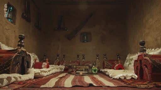 Vue intérieure d'une pièce traditionnelle avec des tapis, des coussins et des objets artisanaux, évoquant l'habitat traditionnel dans une région du Moyen-Orient ou d'Afrique du Nord.