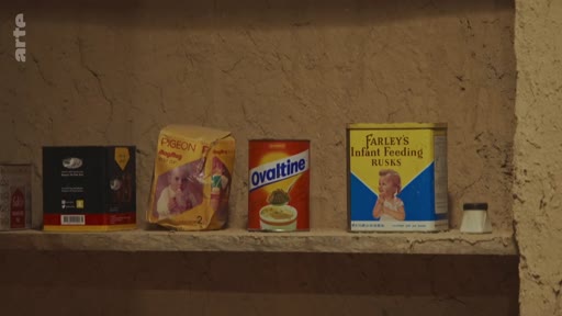 Une étagère contenant des produits de consommation courante, notamment des boîtes de lait infantile Pigeon, une boîte de poudre chocolatée Ovaltine et des biscuits Farley's Infant Feeding Rusks.