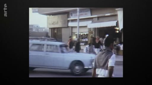 Vue d'archive montrant une rue passante au Qatar vers 1971, avec des voitures anciennes et des passants devant des commerces locaux, illustrant le développement urbain du pays au moment de son indépendance.