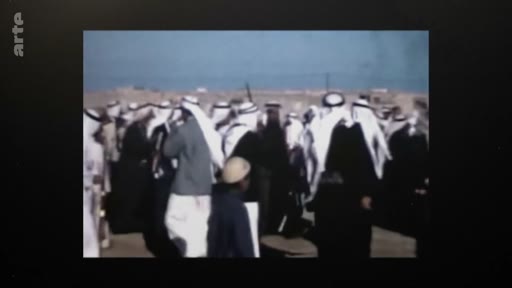 Un groupe d'hommes vêtus de tenues traditionnelles, notamment des keffiehs, réunis en extérieur dans un environnement désertique. Cette image d'archive montre une foule rassemblée, probablement dans un contexte politique ou social au Moyen-Orient.