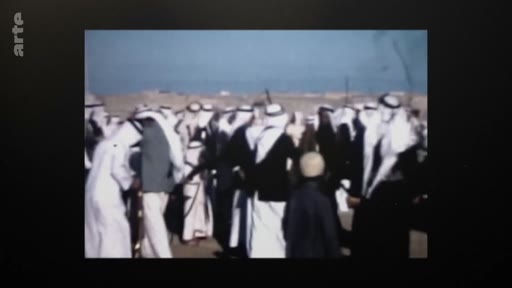 Un groupe d'hommes portant des tenues traditionnelles arabes, incluant des keffiehs et des thobes, rassemblés dans un paysage désertique. Cette image d'archive illustre la vie sociale ou une cérémonie traditionnelle dans une région du Moyen-Orient.