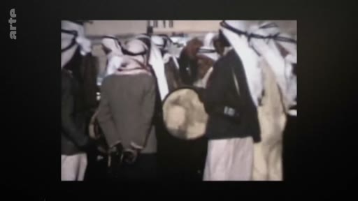 Des hommes vêtus de tenues traditionnelles, incluant des keffiehs, participent à une cérémonie ou un rassemblement culturel, avec un homme jouant d'un tambour au centre.
