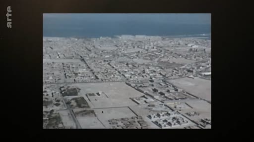 Vue aérienne en noir et blanc d'une ville côtière, probablement une archive historique montrant le développement urbain près du littoral.