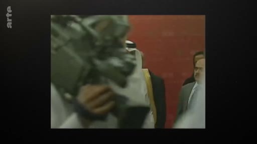 Un caméraman professionnel filme une personnalité politique ou diplomatique portant une tenue traditionnelle arabe lors d'un événement officiel. L'image, de type archive, montre une interaction dans un contexte diplomatique ou politique.
