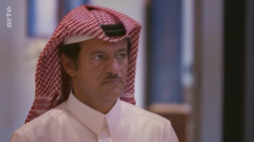 Portrait d'un homme portant une ghutra traditionnelle rouge et blanche, filmé en gros plan lors d'une interview télévisée.