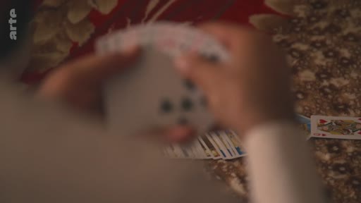 Gros plan sur les mains d'une personne tenant un jeu de cartes à jouer, avec une carte visible sur la table. Le logo de la chaîne Arte est présent dans le coin supérieur gauche.