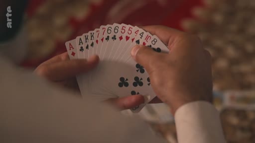 Gros plan sur les mains d'une personne tenant un éventail de cartes à jouer, incluant des as, des rois et des chiffres, lors d'une partie de cartes.