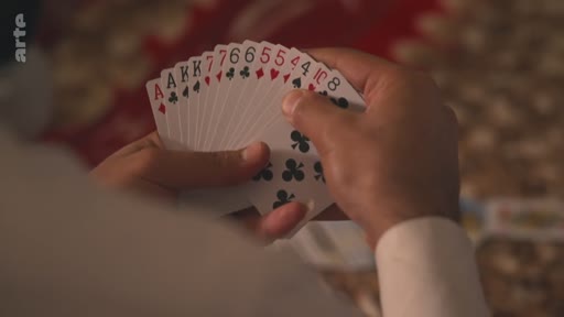 Gros plan sur les mains d'une personne tenant un éventail de cartes à jouer, incluant des as, des rois et des chiffres, lors d'une partie de cartes.