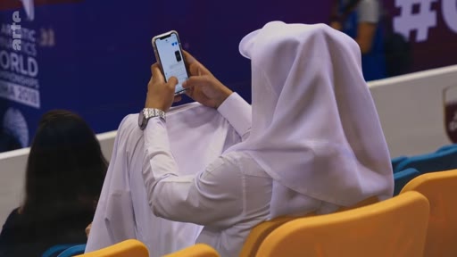 Un spectateur portant une thobe et une ghutra consulte son smartphone dans les tribunes lors des Championnats du monde de gymnastique artistique 2018 à Doha.