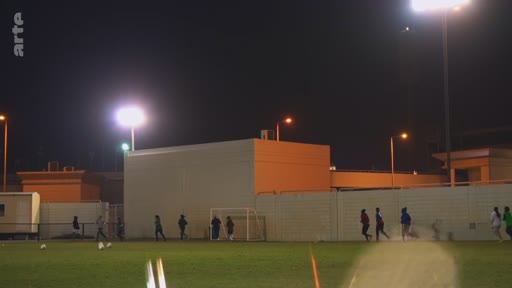 Des joueurs de football effectuent une séance d'entraînement nocturne sur un terrain éclairé par des projecteurs, sous le logo de la chaîne Arte.