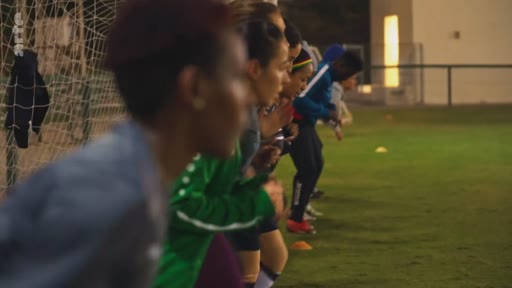 Un groupe de joueuses de football en tenue de sport effectue des exercices physiques sur un terrain de football en extérieur, lors d'une séance d'entraînement en soirée.