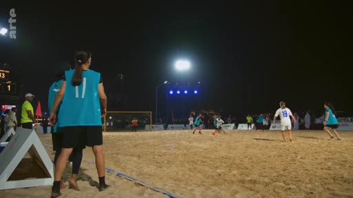 Des joueuses de football de plage s'affrontent sur un terrain sablonneux lors d'un match nocturne, sous les projecteurs. On distingue des joueuses portant des maillots bleus et blancs, avec le logo de la chaîne Arte visible en haut à gauche.