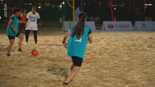 Des joueuses de football en tenue de sport s'entraînent sur un terrain de beach soccer en extérieur lors d'une session nocturne.