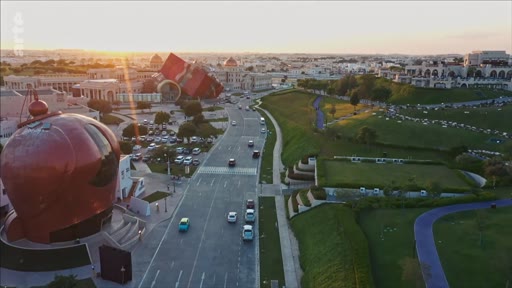 Vue aérienne en plongée du Katara Cultural Village à Doha, au Qatar, au coucher du soleil, mettant en évidence l'architecture distinctive du site et les espaces verts environnants.