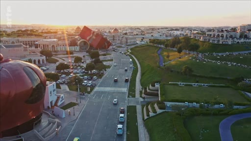 Vue aérienne en plongée du Katara Cultural Village à Doha, au Qatar, montrant l'architecture distinctive, les espaces verts et la circulation routière au coucher du soleil.