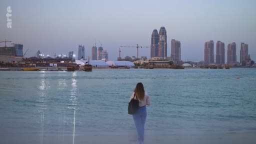 Une femme vue de dos contemple la skyline moderne de Doha, au Qatar, avec ses gratte-ciels illuminés au crépuscule. La scène montre le développement urbain de la ville avec des bateaux traditionnels amarrés près du rivage.