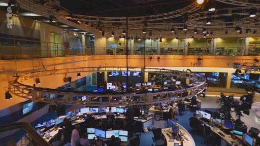 Vue en plongée de la rédaction et du plateau de télévision de la chaîne Arte, montrant les journalistes travaillant sur leurs ordinateurs sous une structure circulaire d'éclairage.
