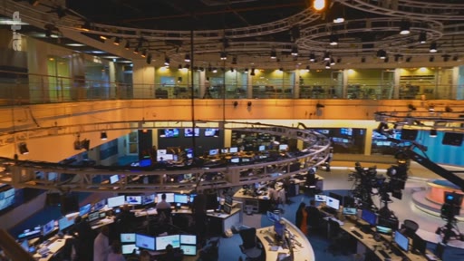 Vue en plongée de la salle de rédaction et du plateau de télévision de Channel 4 News, montrant les journalistes au travail devant leurs écrans et les installations techniques de production.