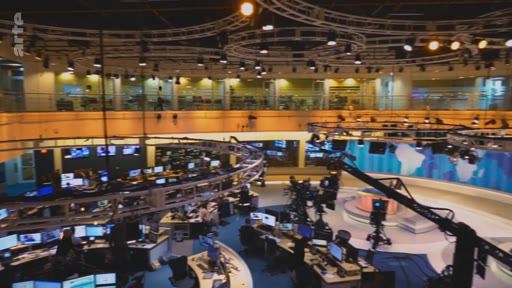 Vue d'ensemble du plateau de télévision de la chaîne Arte, montrant les bureaux de la rédaction, les écrans de contrôle et le décor du studio avec une carte du monde en arrière-plan.