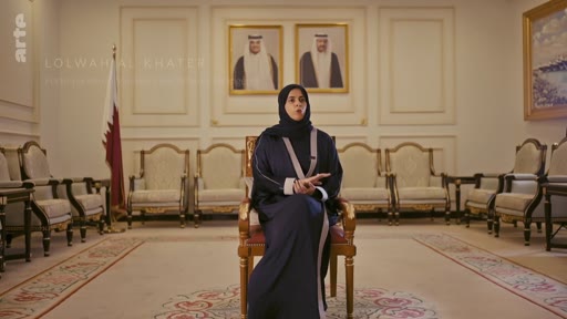 Lolwah Al-Khater, diplomate qatarienne, est interviewée dans un salon officiel orné des portraits des dirigeants du Qatar et du drapeau national.