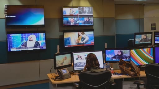 Vue d'une salle de rédaction télévisée avec une employée travaillant devant des écrans d'ordinateur, entourée de multiples moniteurs diffusant des chaînes d'information en continu comme Euronews.