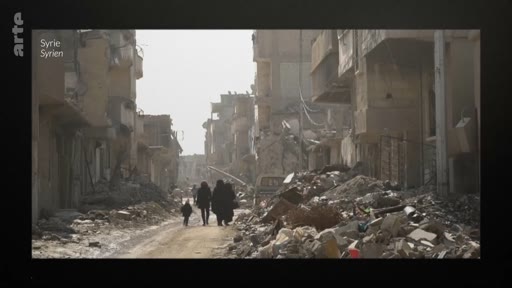 Des civils, dont un enfant, marchent au milieu des décombres et des bâtiments détruits dans une rue en Syrie, illustrant les conséquences dévastatrices du conflit syrien.