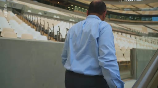 Un homme en chemise bleue marche dans les tribunes désertes du stade de Roland-Garros à Paris. Le site est vide, évoquant la préparation ou la fin d'un tournoi de tennis majeur.