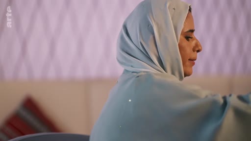 Une femme portant un hijab bleu clair est filmée de profil dans un intérieur lumineux. L'image est issue d'un reportage de la chaîne Arte.