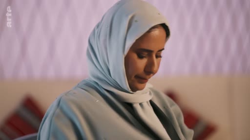 Portrait d'une femme portant un hijab bleu clair, filmée en gros plan dans un cadre intérieur.