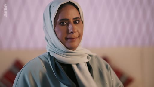 Portrait d'une femme portant un hijab et une tenue traditionnelle, filmée lors d'une interview pour un reportage télévisé.