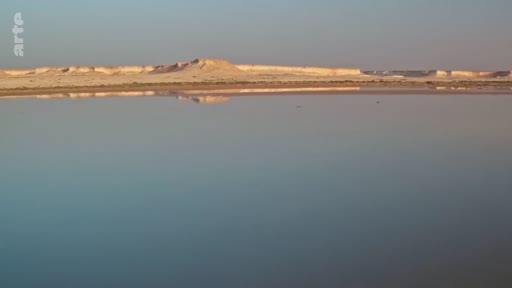 Vue panoramique d'un paysage désertique aride avec des formations rocheuses se reflétant parfaitement dans une étendue d'eau calme, évoquant les paysages du Sahara ou d'une région désertique similaire.