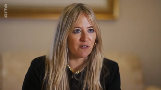 Une femme blonde aux cheveux longs s'exprime face caméra lors d'une interview télévisée, portant un haut noir et un collier doré.