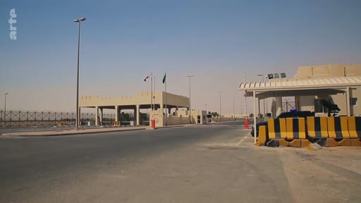 Vue d'ensemble d'un poste-frontière désertique avec des barrières de sécurité et des drapeaux, illustrant les infrastructures de contrôle aux frontières dans une région aride.