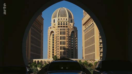 Vue architecturale d'un gratte-ciel avec un dôme, situé à Doha, au Qatar, prise à travers une arche sombre. Ce bâtiment emblématique illustre le développement urbain et l'architecture contemporaine de la capitale qatarienne.