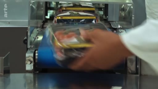 Une main d'ouvrier place des barquettes de viande emballées sous film plastique sur une ligne de production industrielle automatisée dans une usine agroalimentaire.