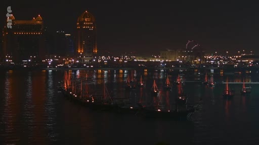 Vue nocturne du port de Doha au Qatar, mettant en avant des boutres traditionnels amarrés sur l'eau avec les gratte-ciels de la ville en arrière-plan.
