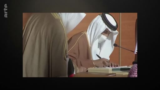 Un homme portant une tenue traditionnelle saoudienne, incluant une ghutra et un agal, signe un document officiel lors d'une cérémonie. Il porte un masque de protection sanitaire, suggérant un contexte lié à la pandémie de COVID-19.