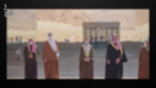 Plusieurs officiels portant des tenues traditionnelles arabes, dont des thobes et des ghutras, se tiennent debout lors d'une cérémonie officielle en extérieur devant un bâtiment en pierre.