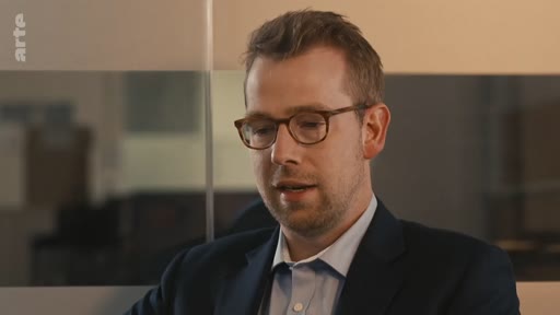 Un homme portant des lunettes et une veste de costume s'exprime lors d'une interview télévisée sur la chaîne Arte.