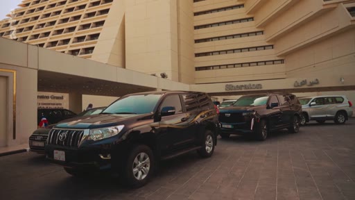 Plusieurs voitures, dont un Toyota Land Cruiser Prado et un Cadillac Escalade, sont stationnées devant l'entrée de l'hôtel Sheraton.