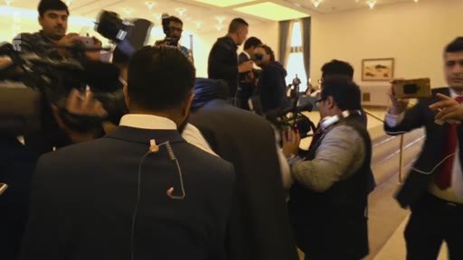 Des journalistes, des cameramen et des photographes sont rassemblés dans une salle de conférence pour couvrir un événement médiatique. On aperçoit plusieurs professionnels des médias équipés de caméras et de matériel d'enregistrement.