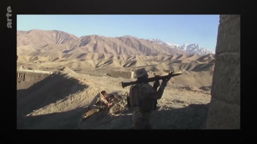 Des soldats équipés d'armes, dont un lance-roquettes, observent le terrain dans une région montagneuse désertique, évoquant les opérations militaires en Afghanistan.