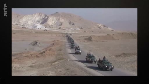Un long convoi de pick-ups militaires circule en file indienne sur une route asphaltée traversant un paysage désertique et montagneux. Cette image illustre des opérations de patrouille ou de déplacement de troupes dans une zone de conflit ou une région isolée.