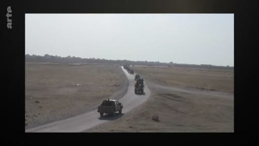Un convoi de pick-ups et de véhicules tout-terrain progresse en file indienne sur une route goudronnée traversant une vaste étendue désertique. Cette image d'archive illustre des déplacements de groupes armés ou de forces militaires dans des zones reculées.