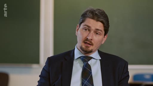 Un homme en costume et cravate, portant une barbe courte, est filmé en gros plan lors d'une interview sur le plateau de la chaîne Arte.