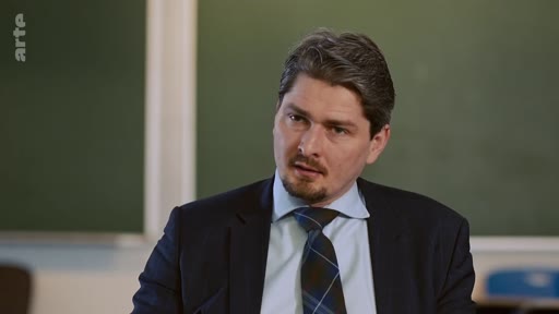 Un homme en costume et cravate, portant une barbe courte, est filmé en gros plan lors d'une interview sur le plateau de la chaîne Arte.